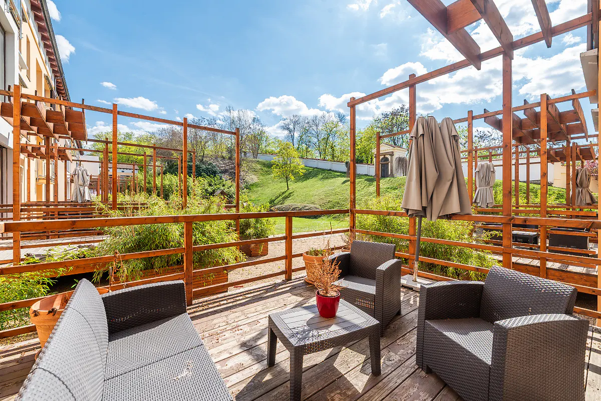 Outdoor patio with wicker furniture, wooden pergola, and view of green landscape under a blue sky.