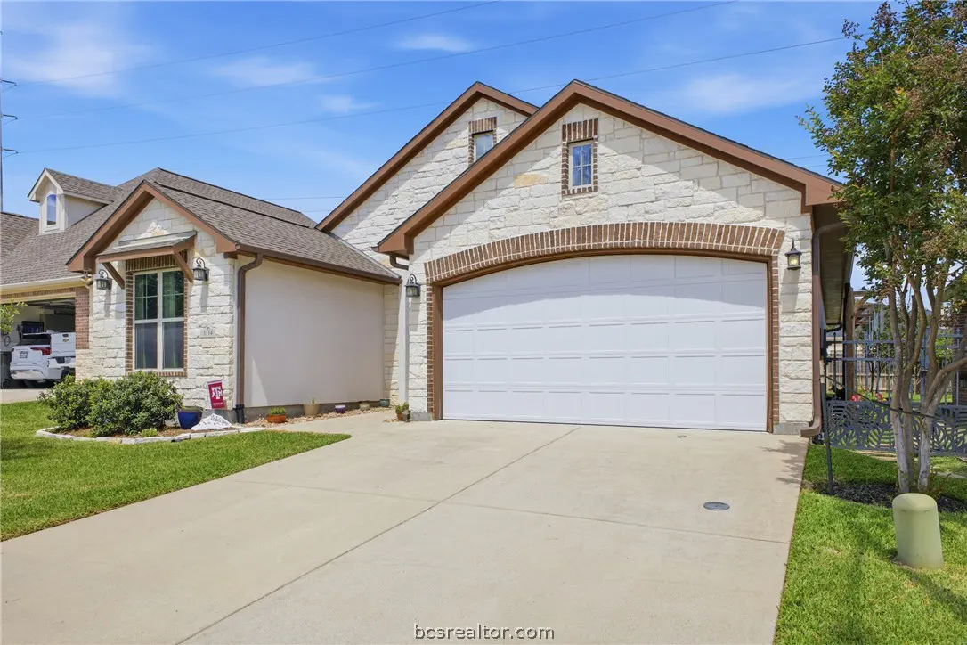 Exterior of a one-story house with a white garage door, stone facade, brown trim, and a concrete driveway.