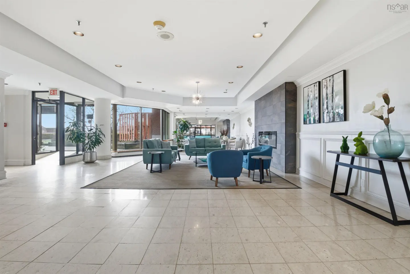 Bright lobby with blue sofas and chairs on a gray rug. A fireplace and console table with decor are on the right.