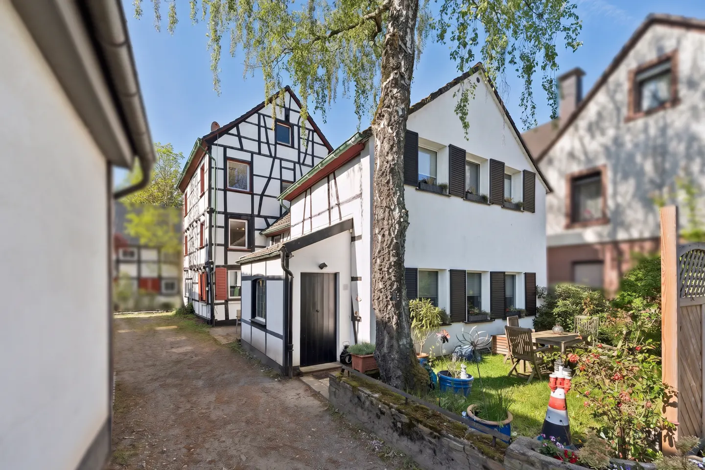 Exterior view of white, half-timbered houses with black shutters and a green lawn with a table and chairs.