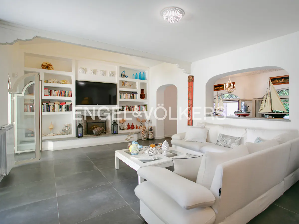 Bright living room with white sofa, coffee table, built-in shelves, fireplace, and nautical decor on gray tile floors.