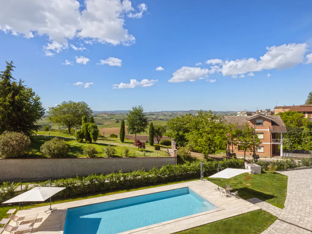 A sunny view of a pool with lounge chairs, a green lawn, and a distant landscape of rolling hills.
