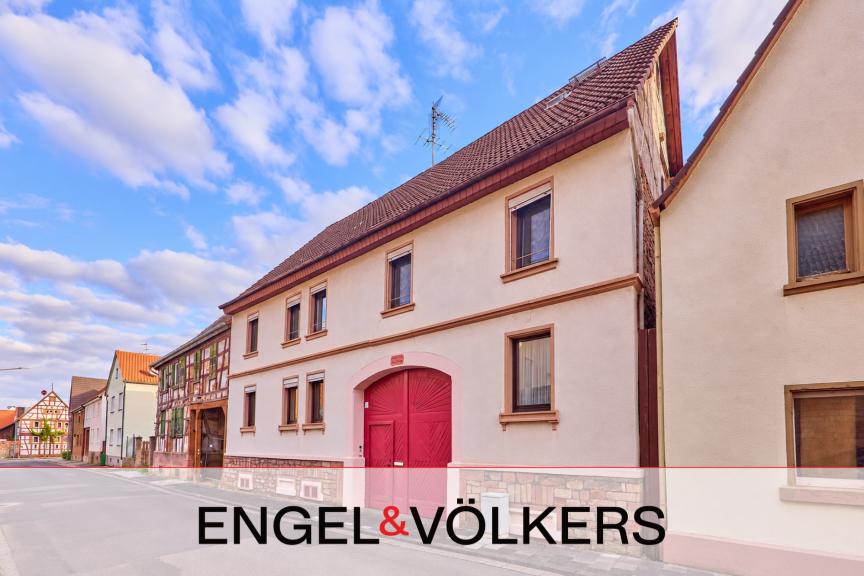 A two-story cream-colored house with a prominent red arched gate and brown roof, situated on a quiet European street. [AI-generated text]