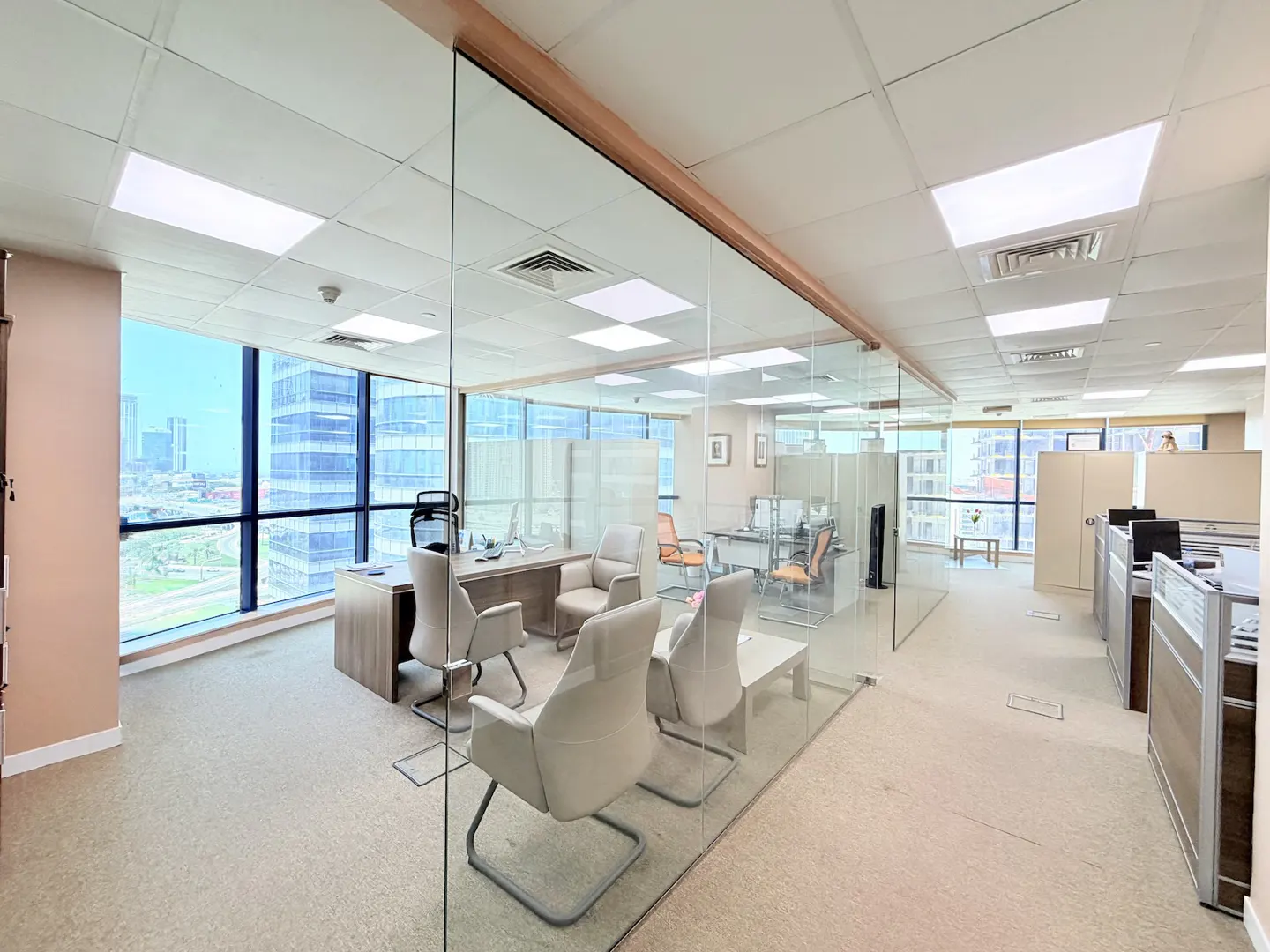 Bright office space with glass-walled conference room, beige carpet, and city views from large windows.