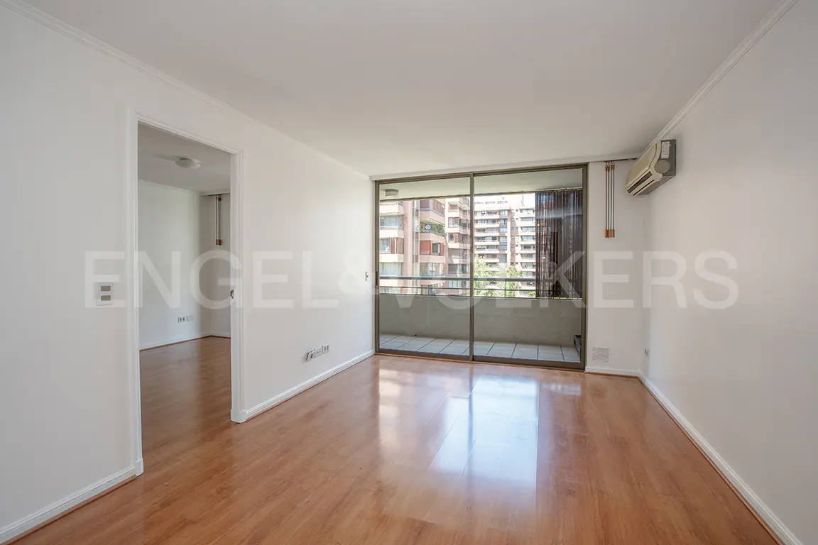 Bright, empty room with wood floors, white walls, and a sliding glass door to a balcony with a city view.