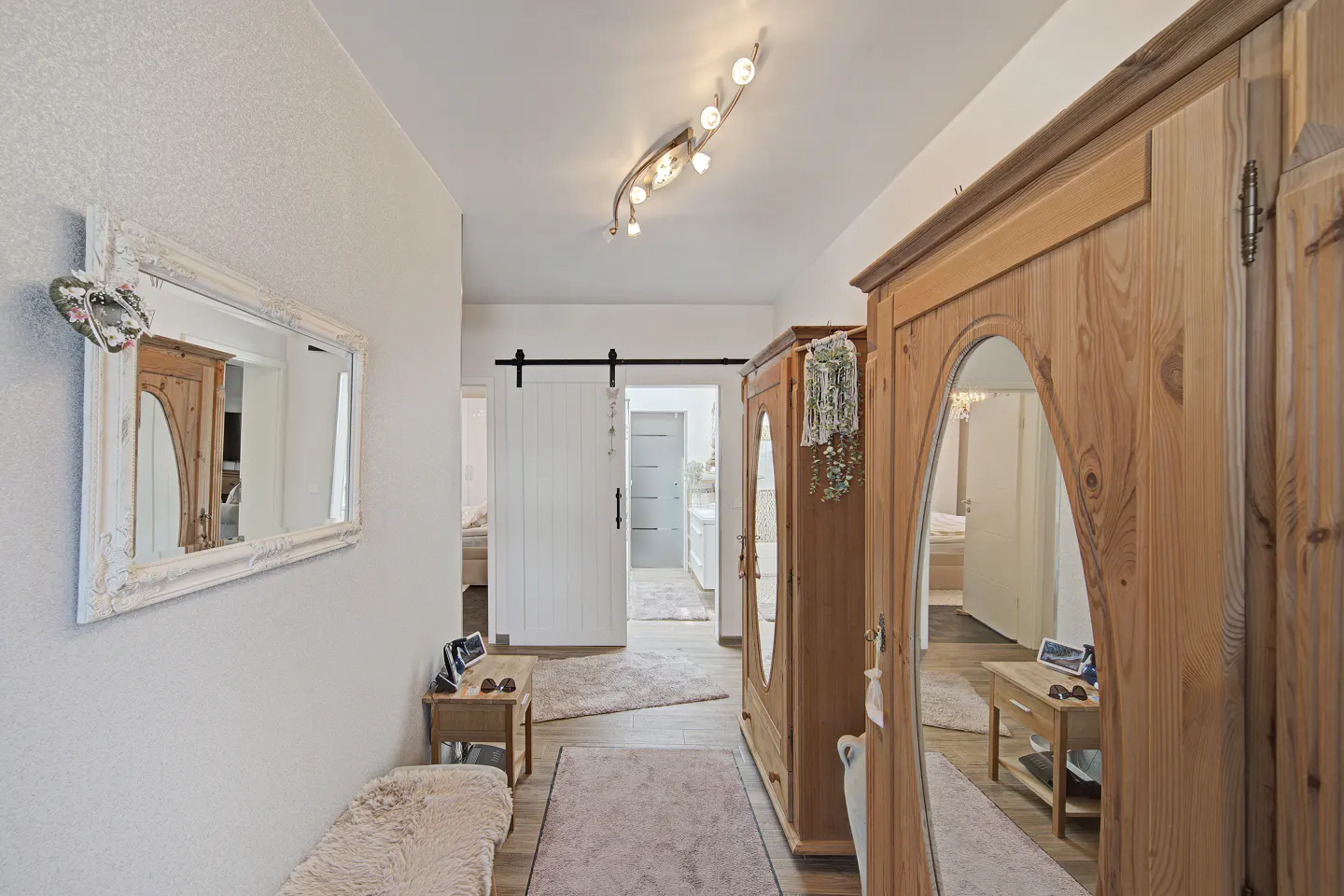 Hallway with light walls, wooden wardrobes with mirrors, and a white sliding door. A mirror hangs on the wall.