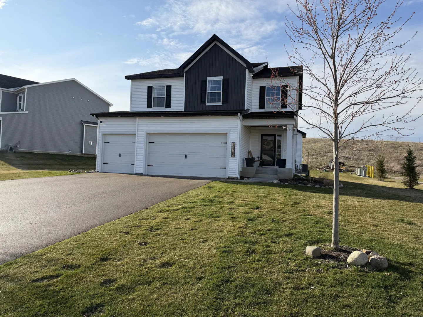 Two-story house with white siding, black trim, and a two-car garage. A tree stands in the front yard.