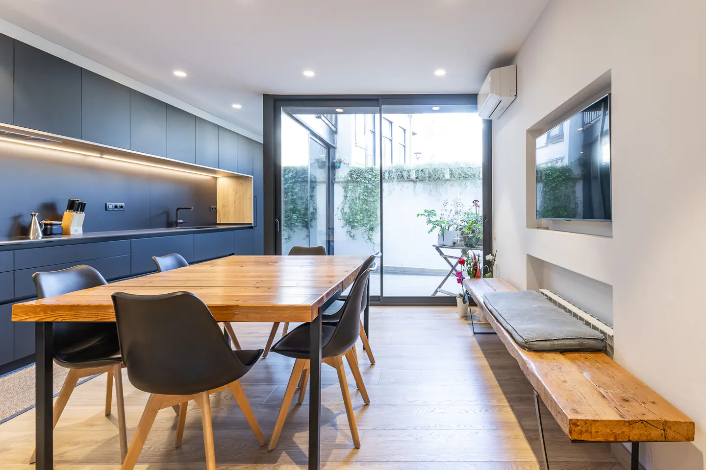 Modern kitchen and dining area with a wooden table, black chairs, and sliding glass doors to a patio.