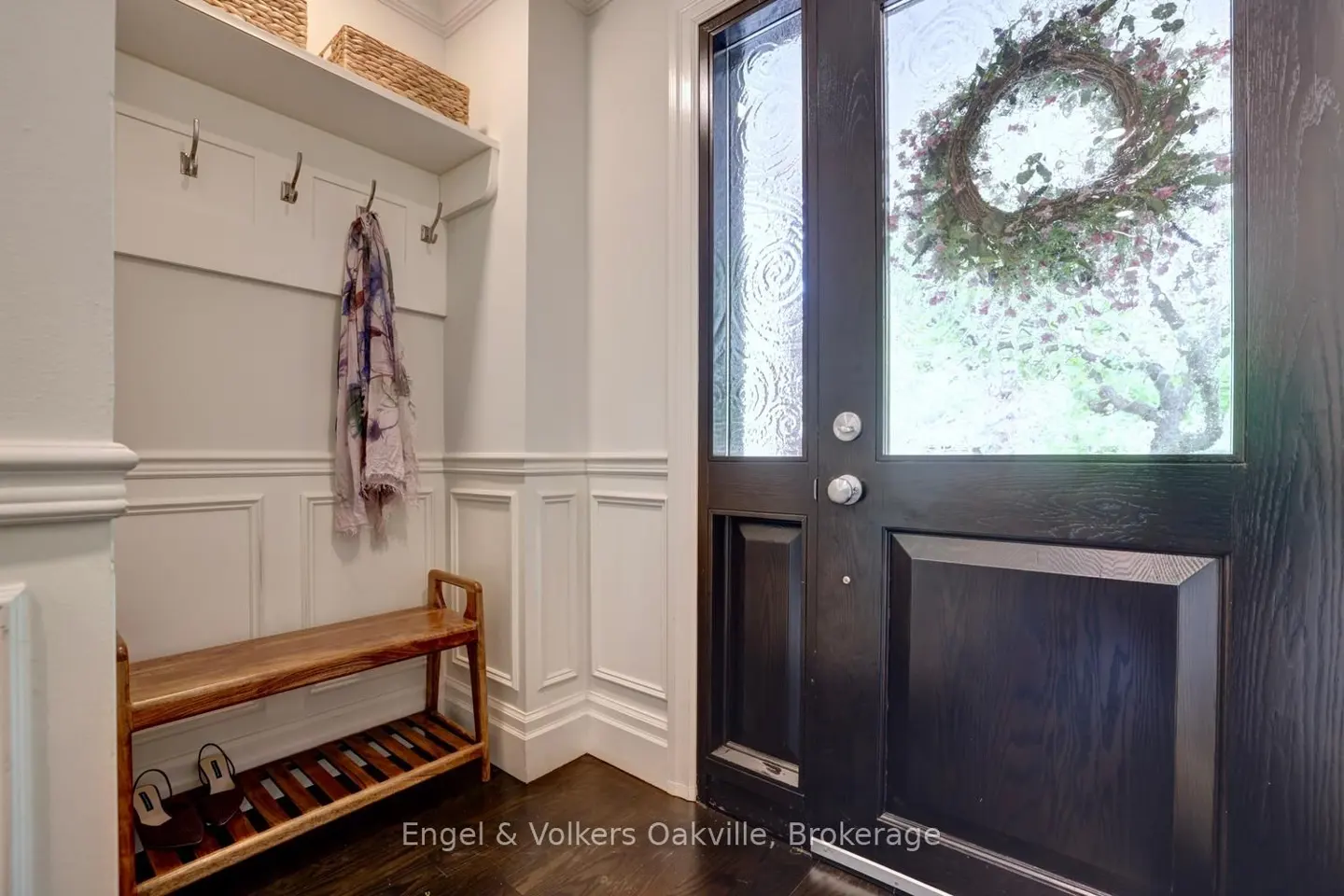 Entryway with white wainscoting, a wooden bench, coat hooks, and a dark wood front door with a floral wreath.