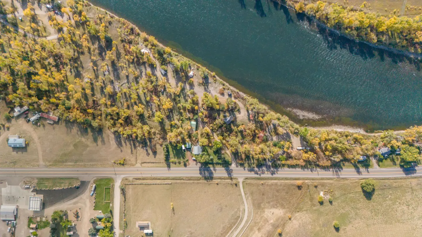 Aerial view of a river winding past a wooded area, a road, and rural properties with autumn-colored trees.