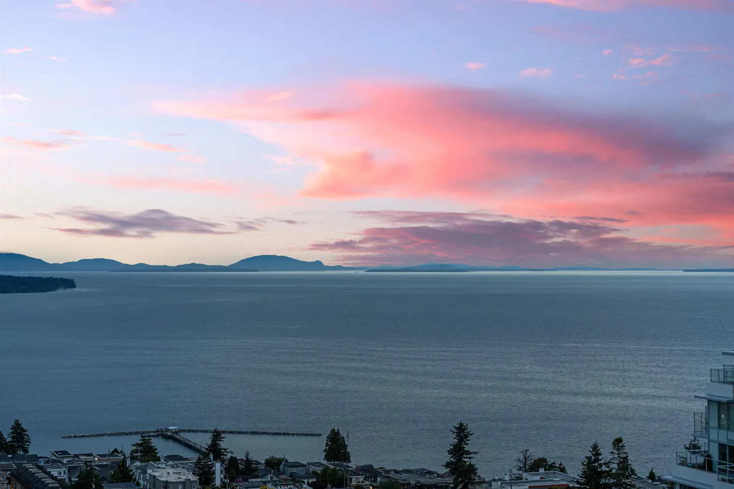 Sunset view of ocean with pink clouds, islands in the distance, and a pier in the foreground.
