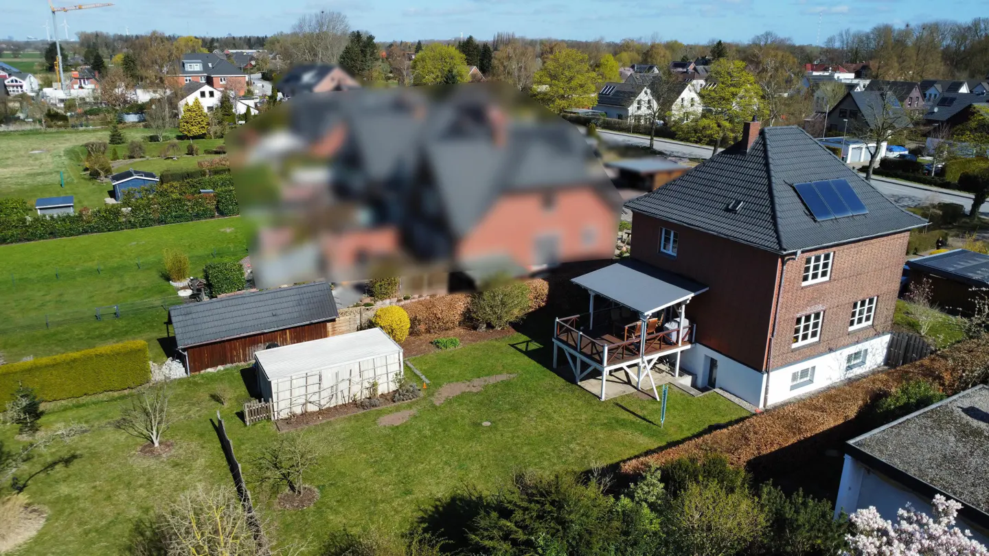 Aerial view of a red brick house with a gray roof and solar panels, a white porch, and a green lawn.