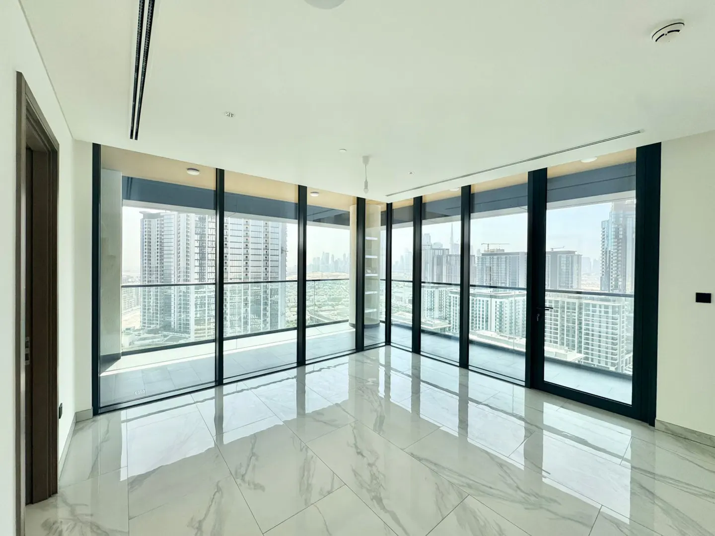 Bright, empty room with marble floors and floor-to-ceiling windows showing a city skyline.