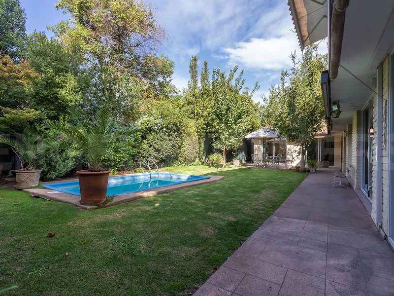 A backyard with a blue swimming pool, green grass, trees, and a patio with a gazebo.