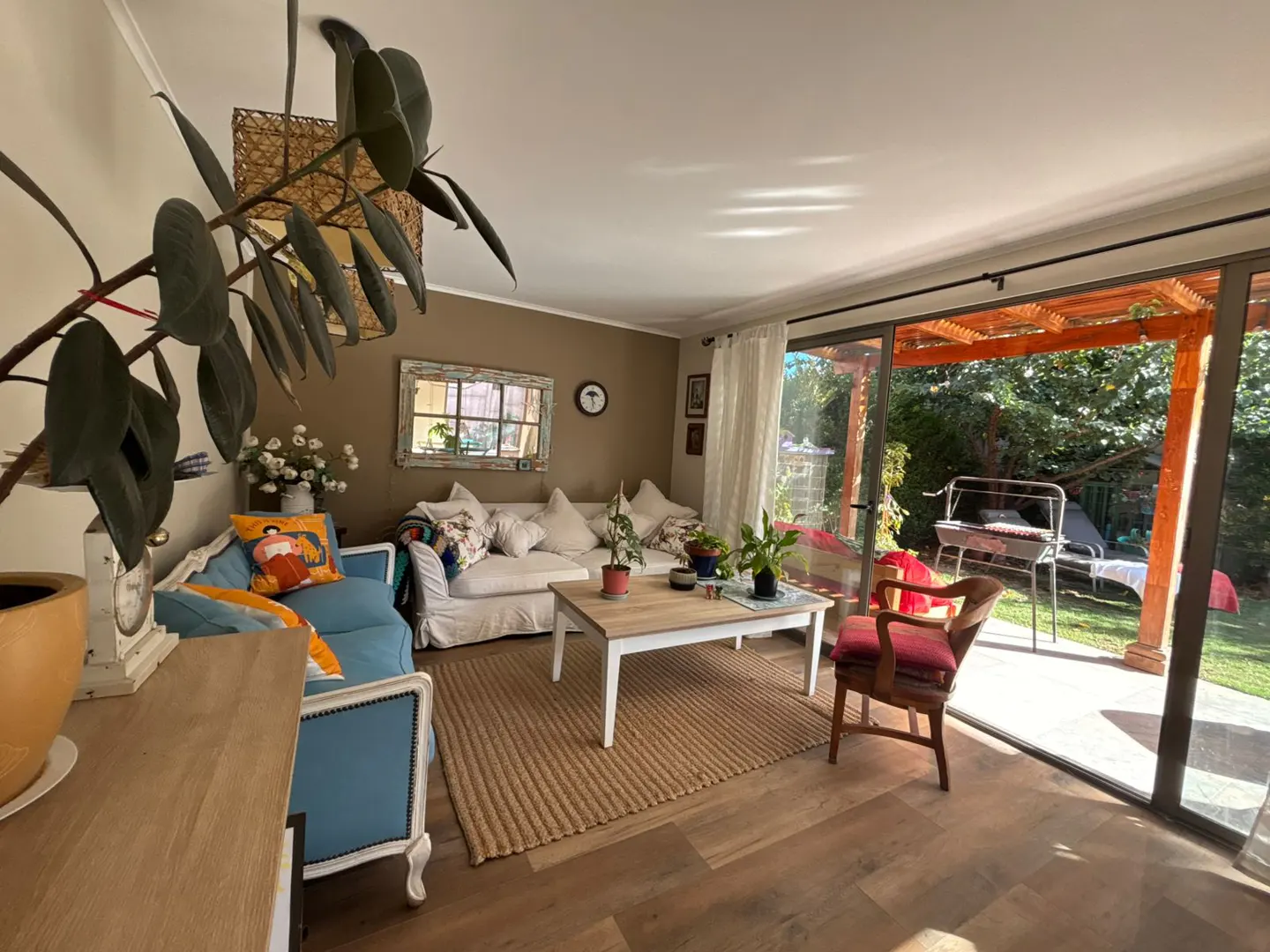 Living room with wood floors, a white sofa, a blue loveseat, and a jute rug. Sliding glass doors lead to a patio and green lawn.