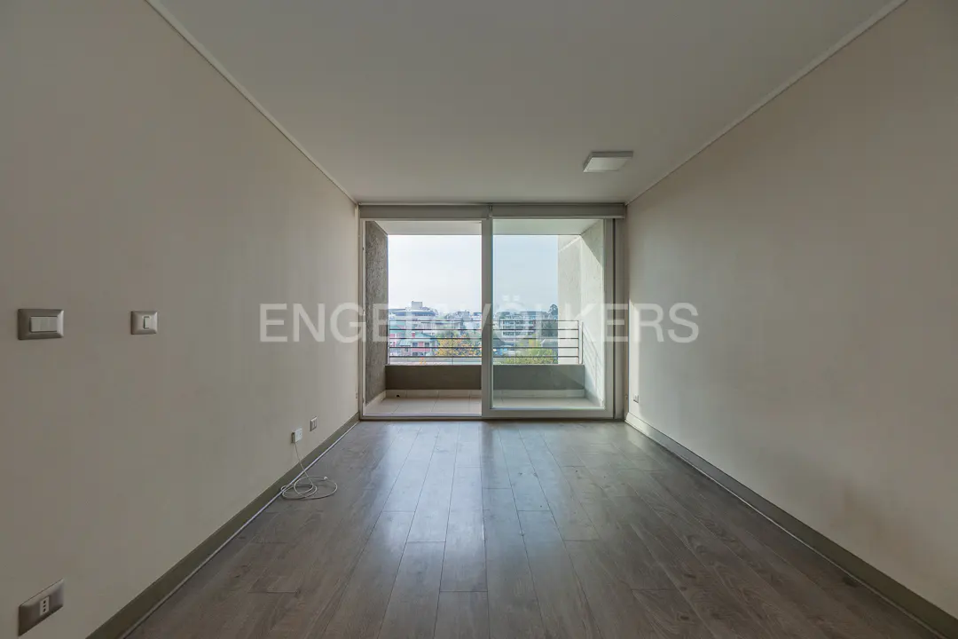 Empty room with gray wood floors, white walls, and a sliding glass door to a balcony with a city view.