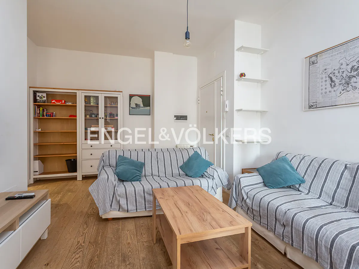 Living room with hardwood floors, two sofas with striped covers and teal pillows, and a wooden coffee table. White walls and built-in shelves.