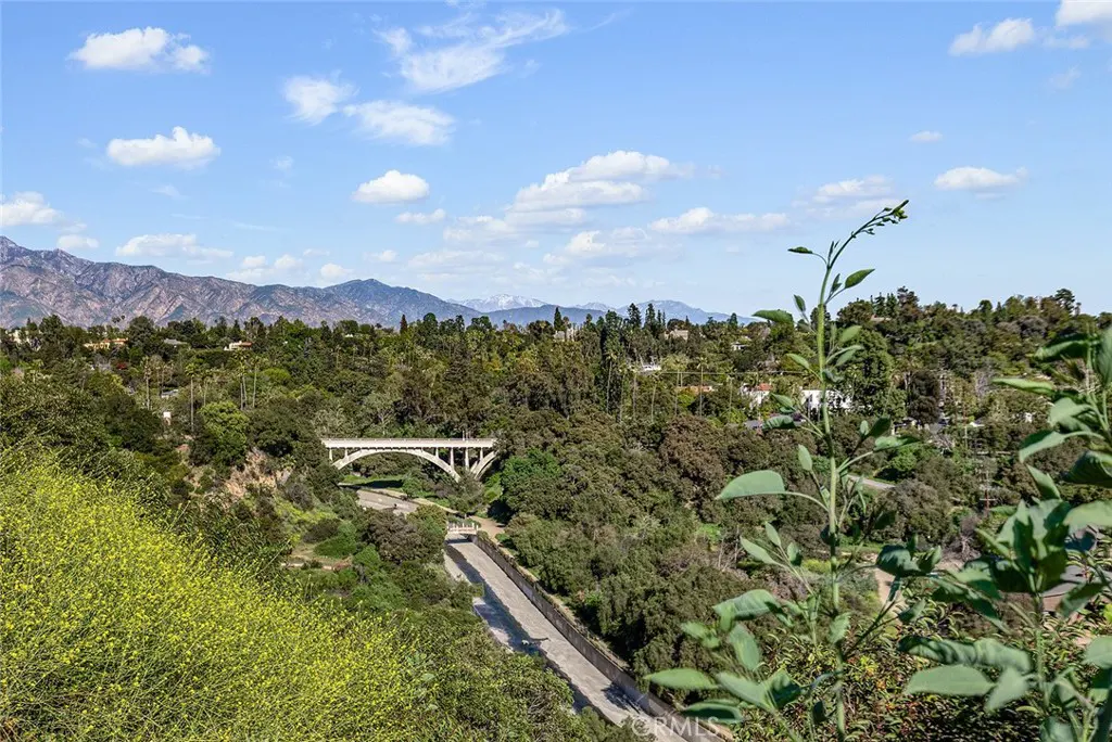 Scenic view of a white bridge spanning a green valley, with mountains in the background under a blue sky with scattered clouds.