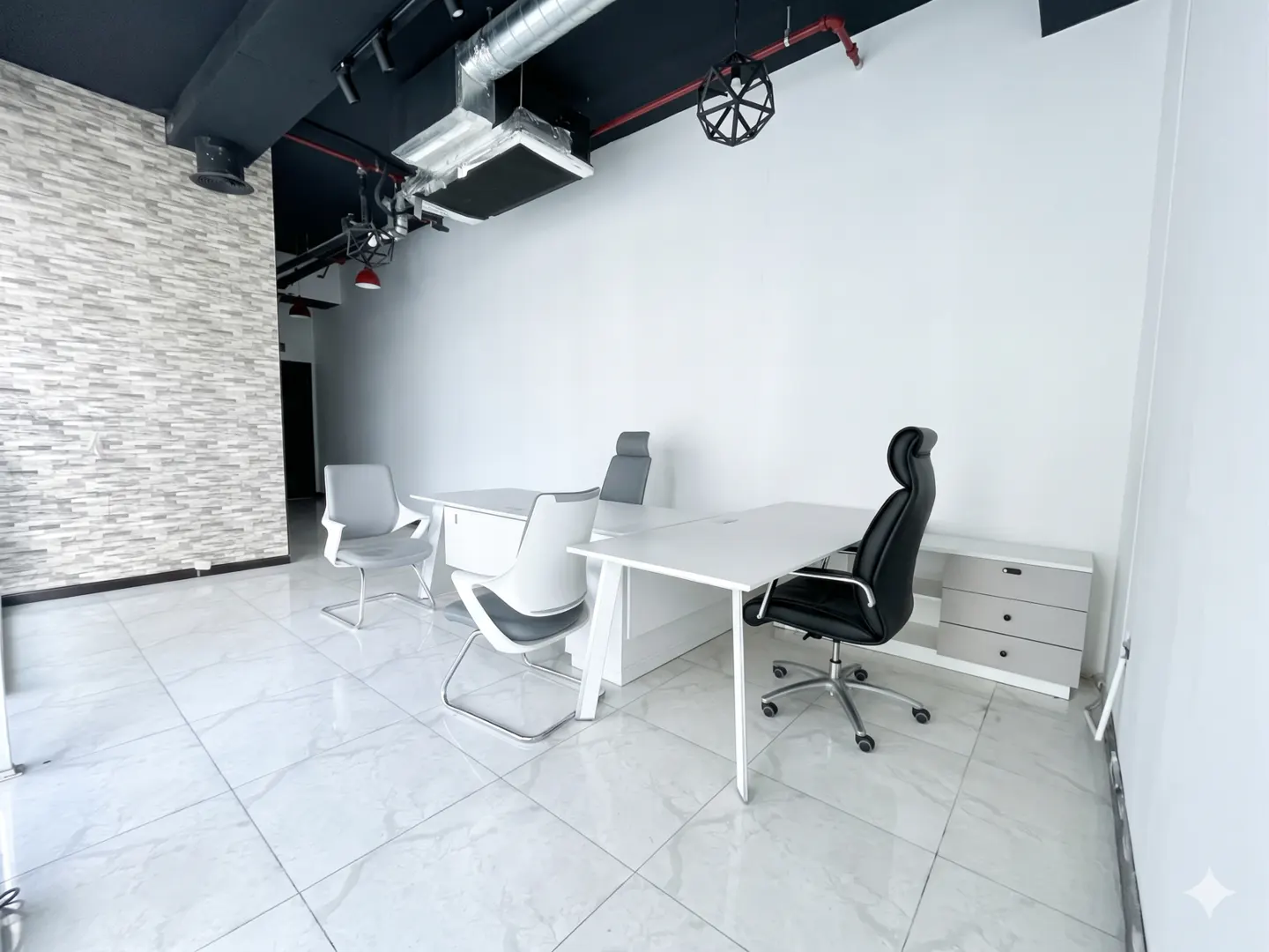 Bright office space with white walls, marble floors, and a black ceiling. Desks with gray and black chairs are arranged in the room.