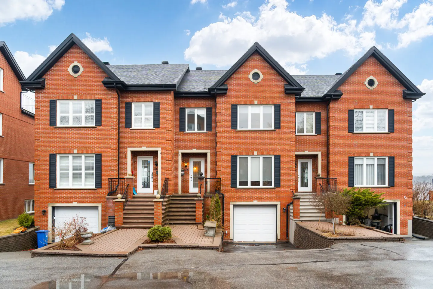Three-story red brick townhouses with black shutters and gray roofs on a cloudy day.