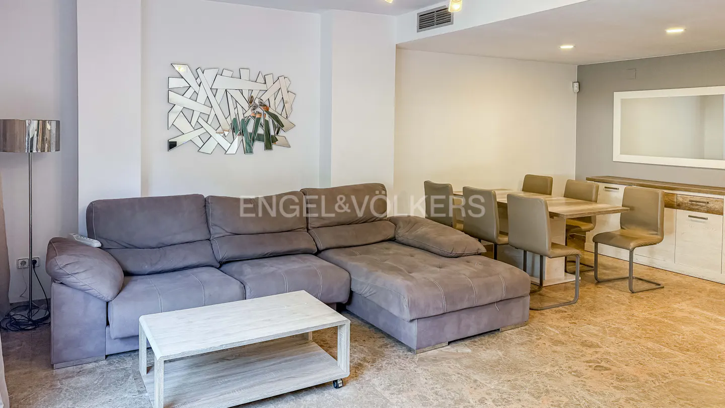 Living room with gray sectional sofa, white coffee table, dining table with six chairs, and modern mirror art.