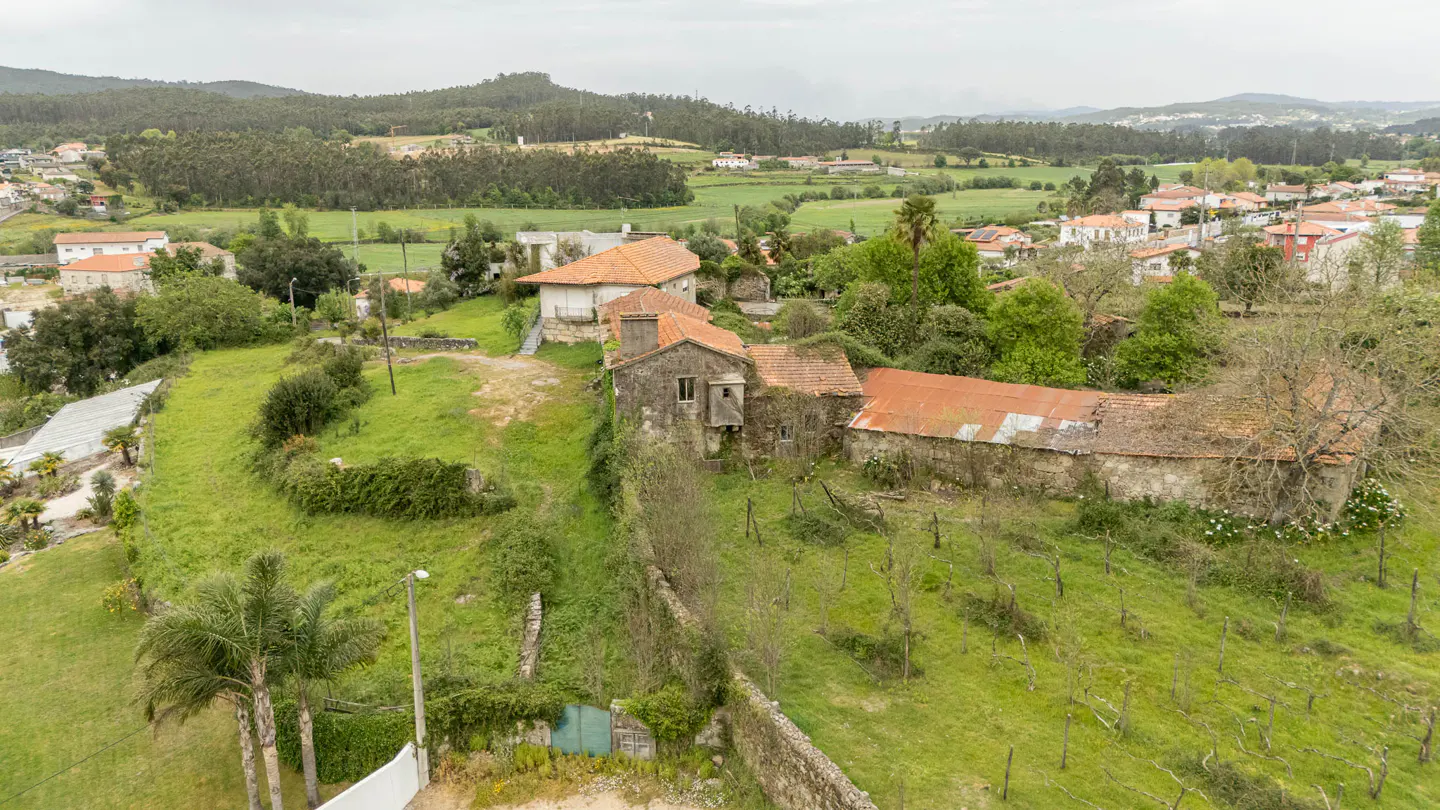 Aerial view of a stone farmhouse with a red tile roof, surrounded by green fields and trees in a rural setting.