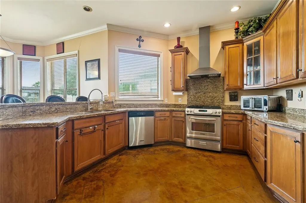 A kitchen with wood cabinets, granite countertops, and stainless steel appliances. A window with blinds is above the sink.