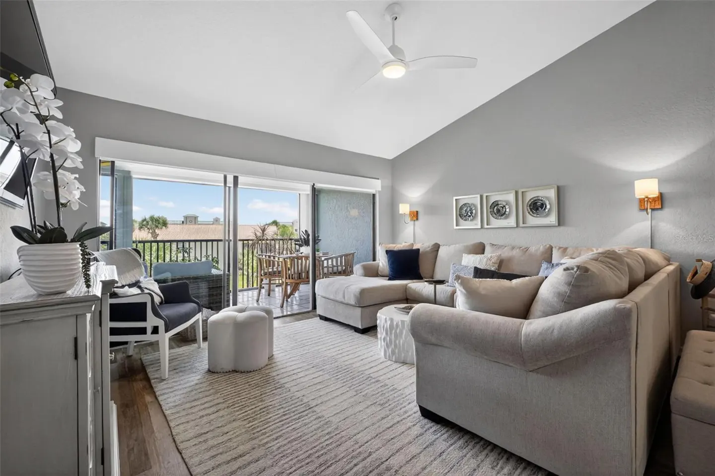 Modern living room with a large beige sectional, gray walls, ceiling fan, and sliding doors opening to a balcony.