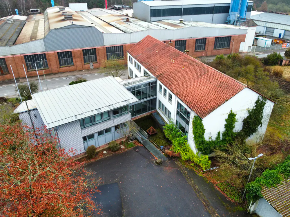 Aerial view of two white buildings connected by a glass walkway, with a red-tiled roof on one and a silver roof on the other.