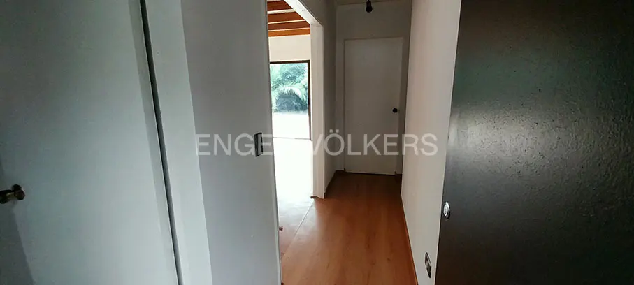 Hallway with wood floors, white walls, and doors. A view to the outside shows green foliage. Engel & Völkers logo is visible.