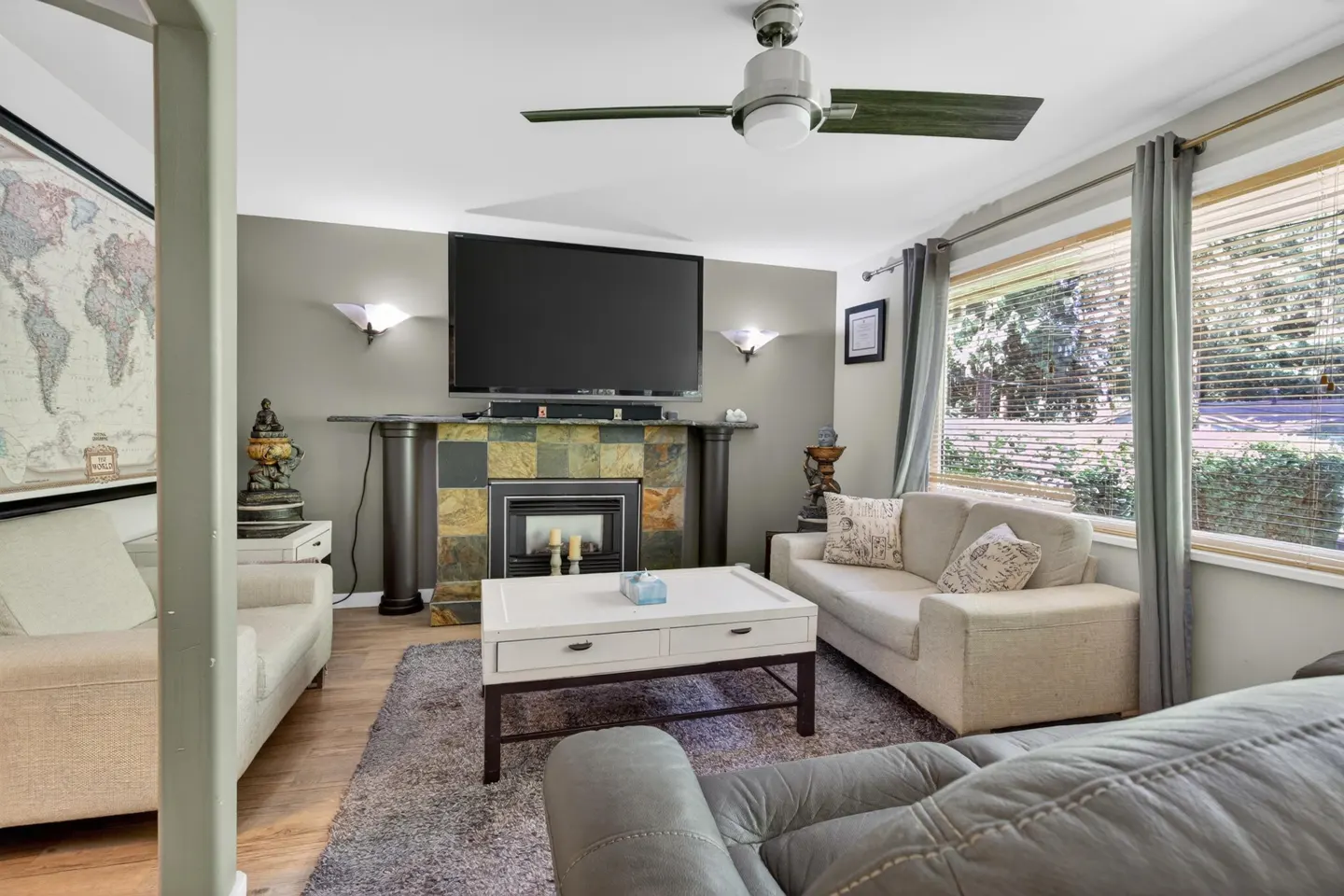 Living room with a stone fireplace, wall-mounted TV, white coffee table, and beige sofas on a grey area rug.
