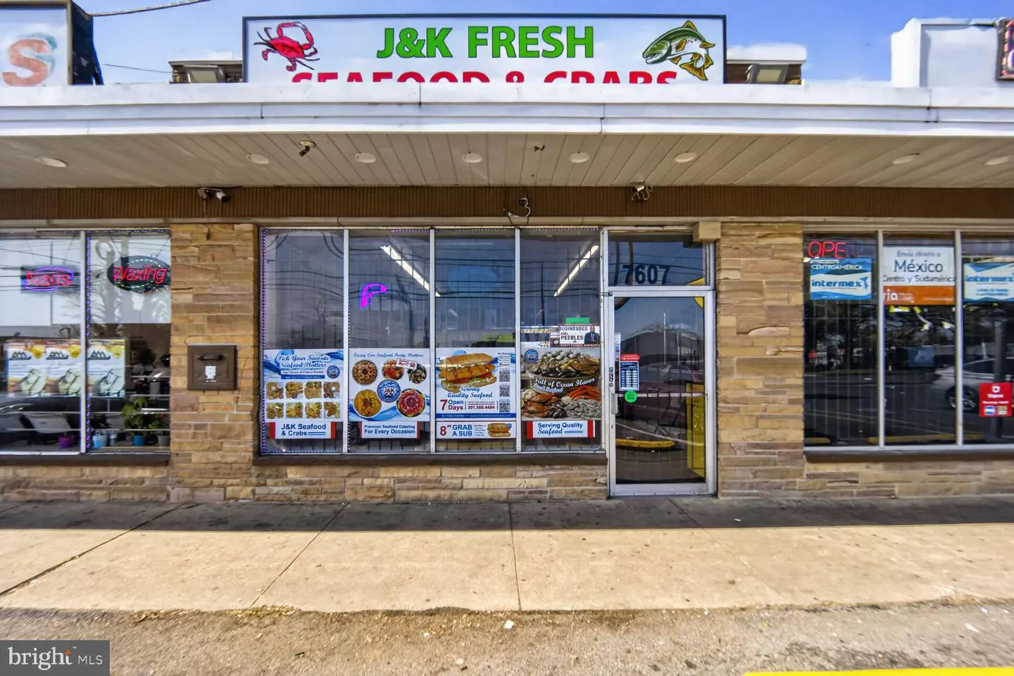 Exterior view of J&K Fresh Seafood & Crabs store with a tan brick facade and large windows displaying menu items.