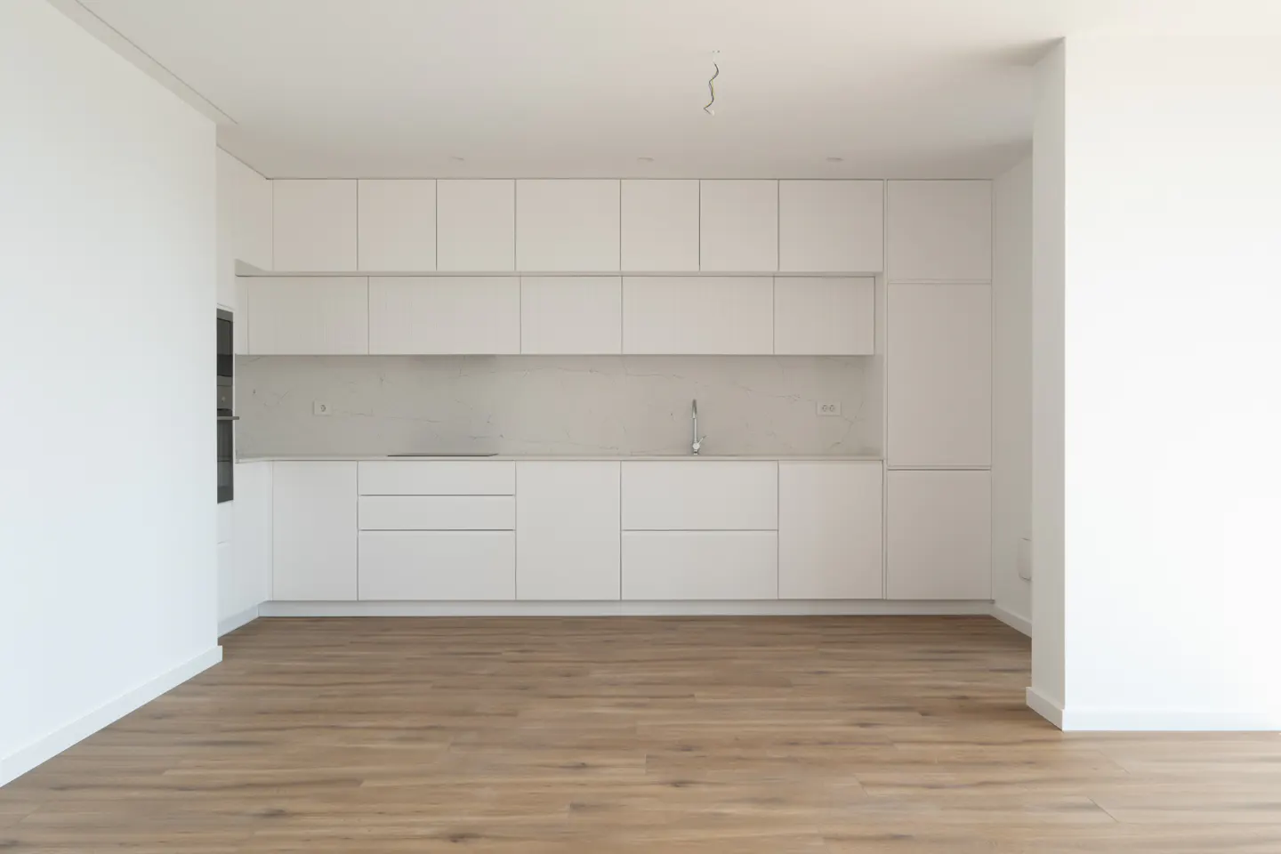 Bright, empty kitchen with white cabinets, marble backsplash, and wood-look flooring.