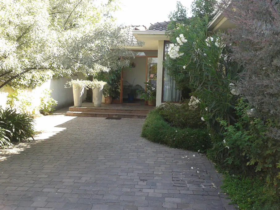 Front exterior of a house with a brick driveway and lush greenery. Two large planters flank the front steps.