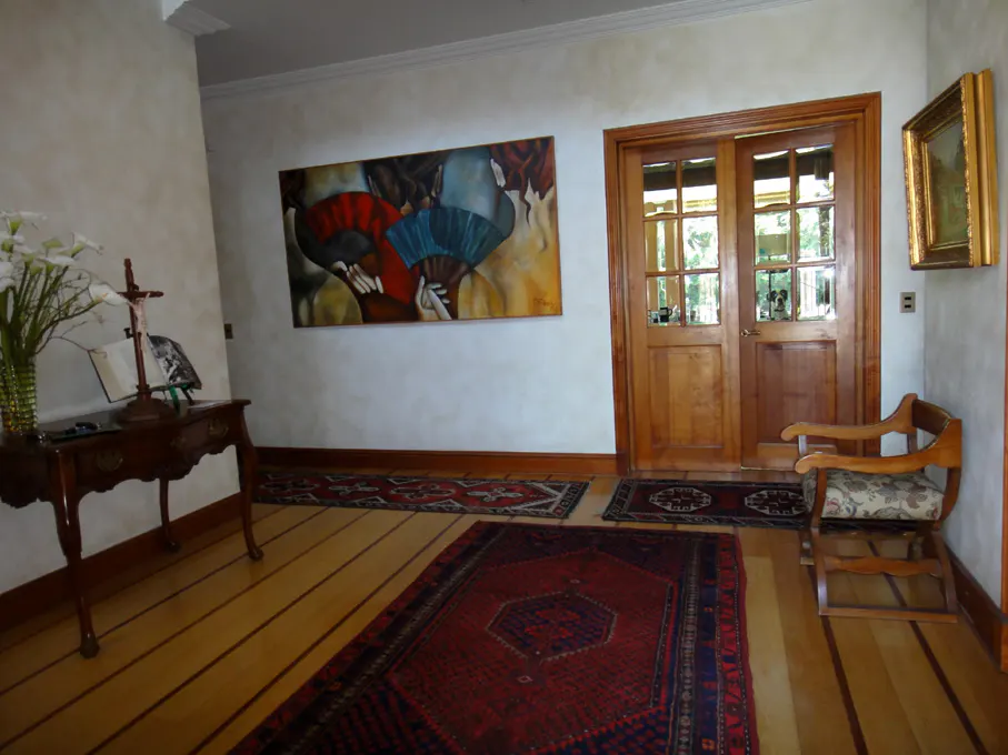 Interior view of a home foyer with hardwood floors, rugs, art, and a wooden chair.