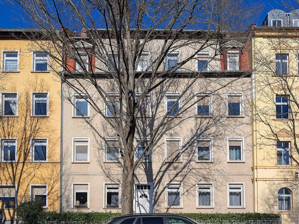 Row of multi-story apartments in yellow and beige, with a bare tree casting shadows on the facade.
