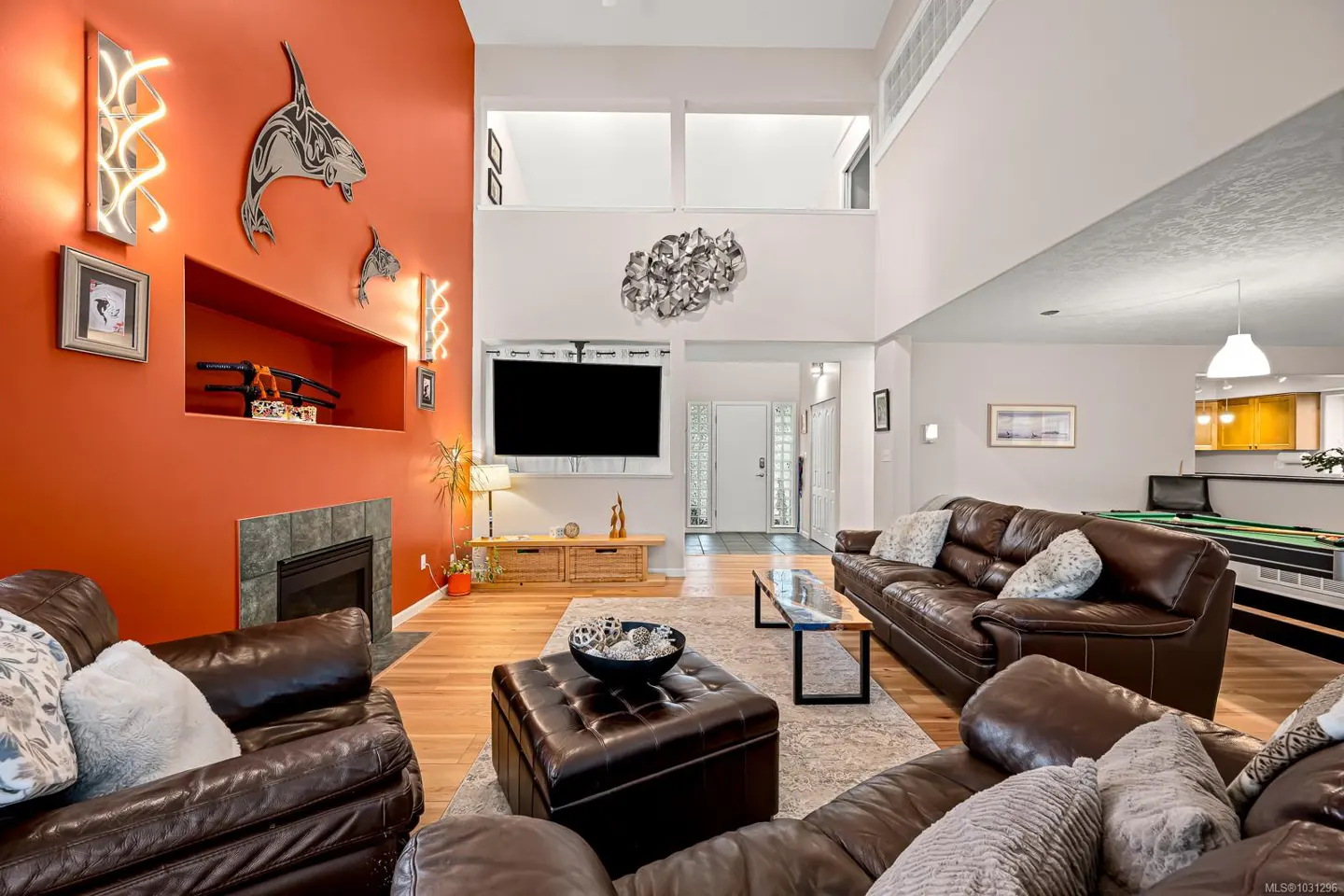 A living room with brown leather sofas, a fireplace, and orange accent wall with orca art.