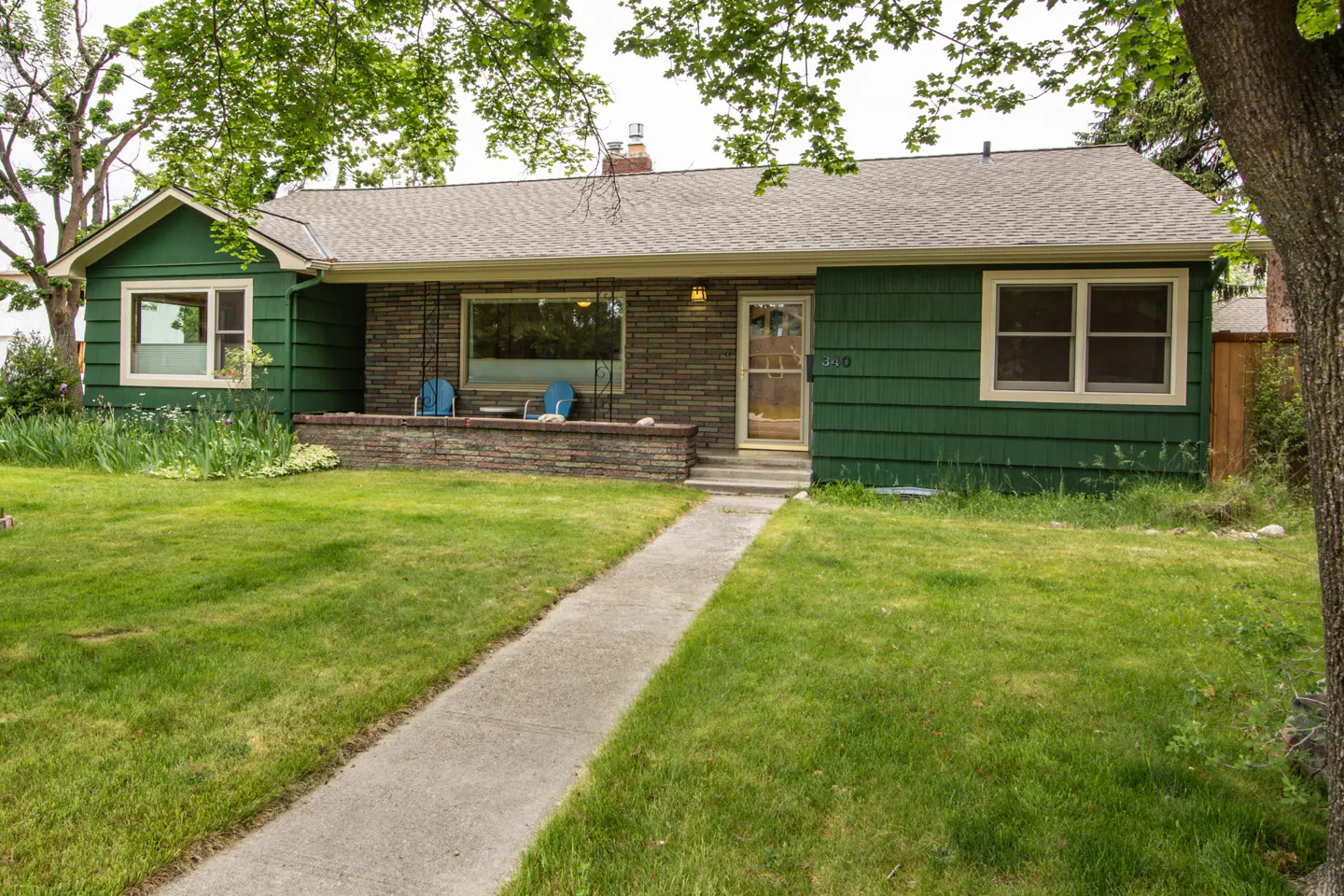 Single-story green house with a stone facade, front porch, and a concrete walkway leading through a grassy yard.