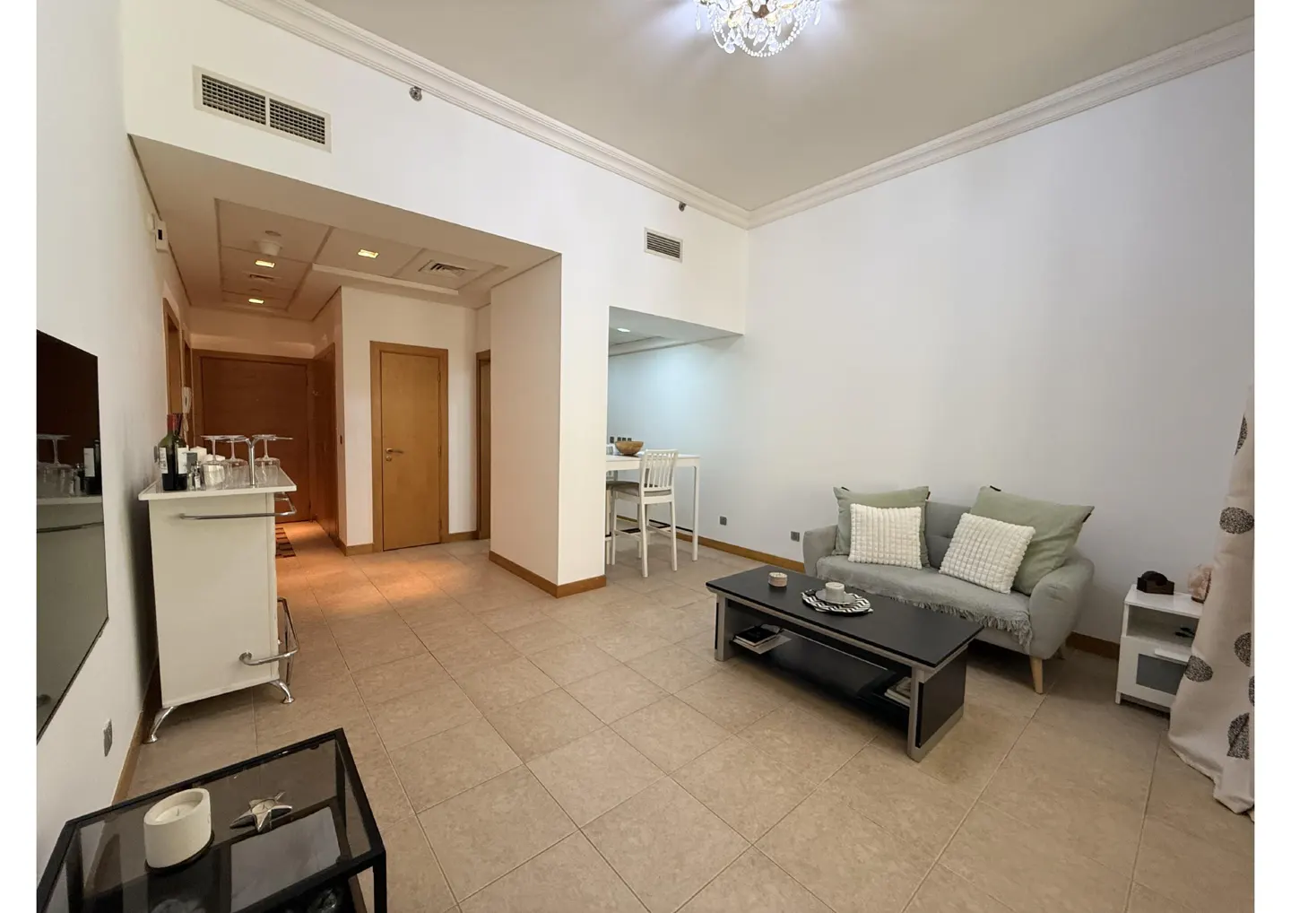 A bright living room with a gray sofa, black coffee table, and white bar with wine glasses.