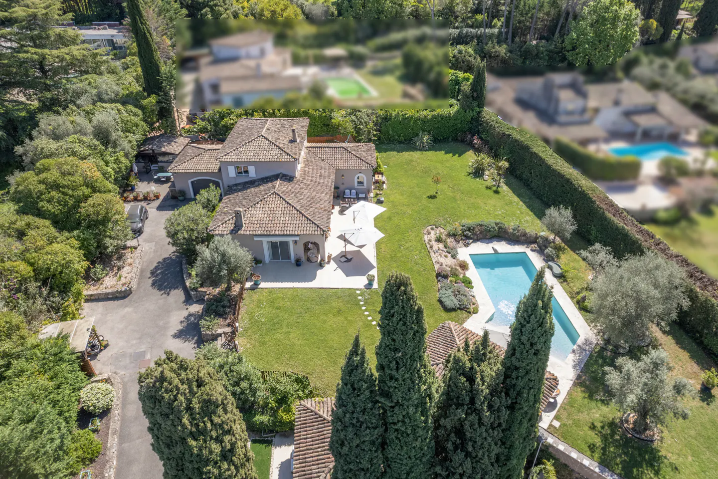 Aerial view of a gray house with a terracotta tile roof, a pool, and green landscaping.