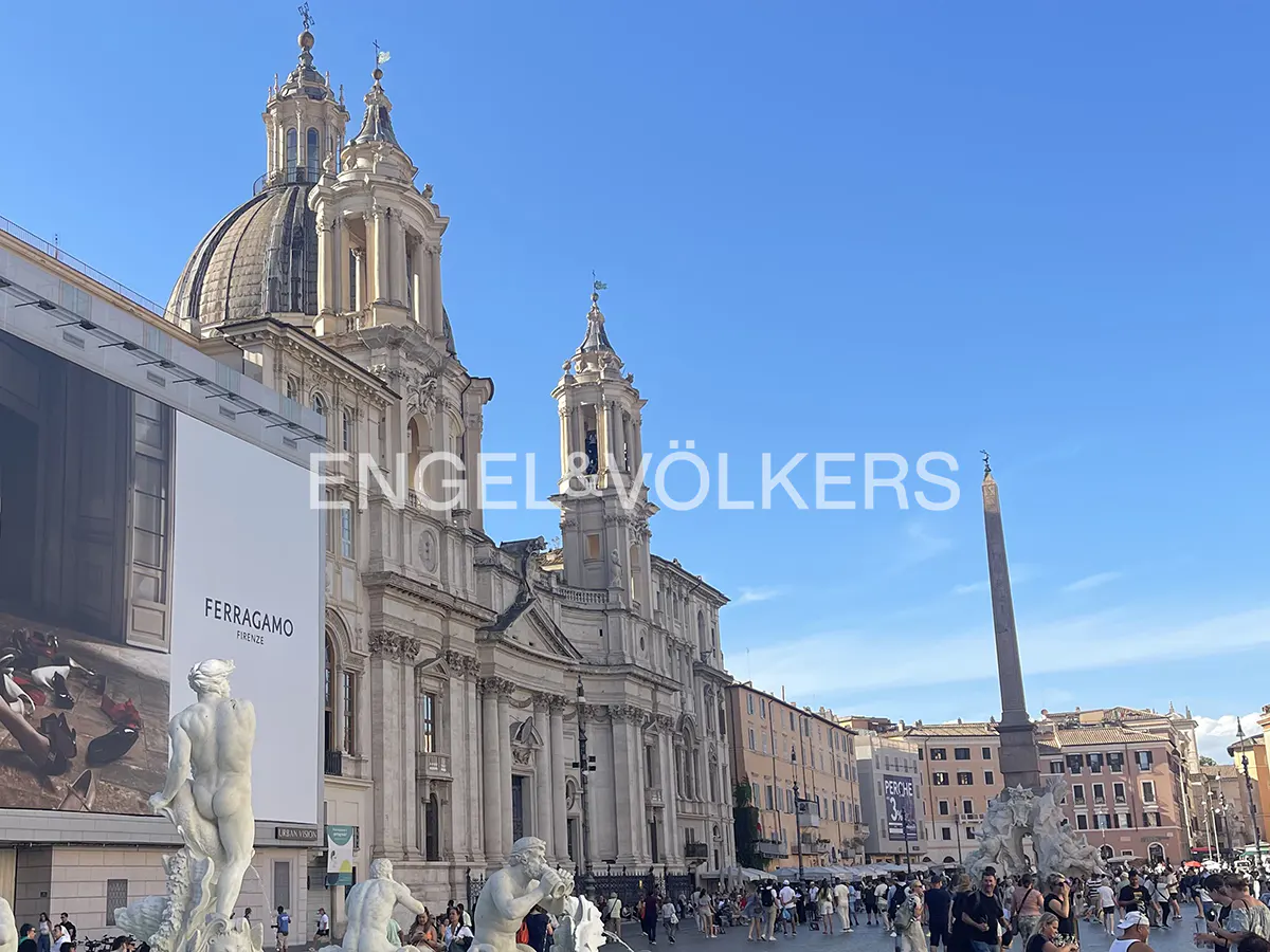 Piazza Navona, Rome, Italy, with the Fountain of Neptune, an obelisk, and the Church of Sant'Agnese in Agone under a blue sky.