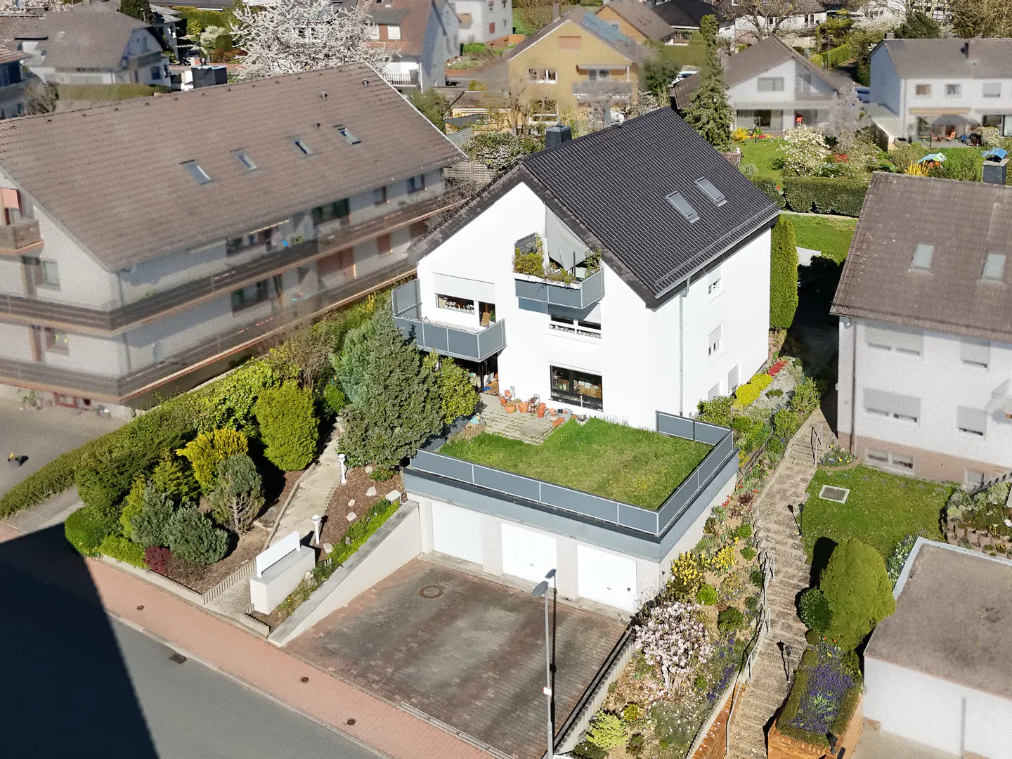 Aerial view of a modern white house with a dark gray roof, balconies, and a green roof over the garage.
