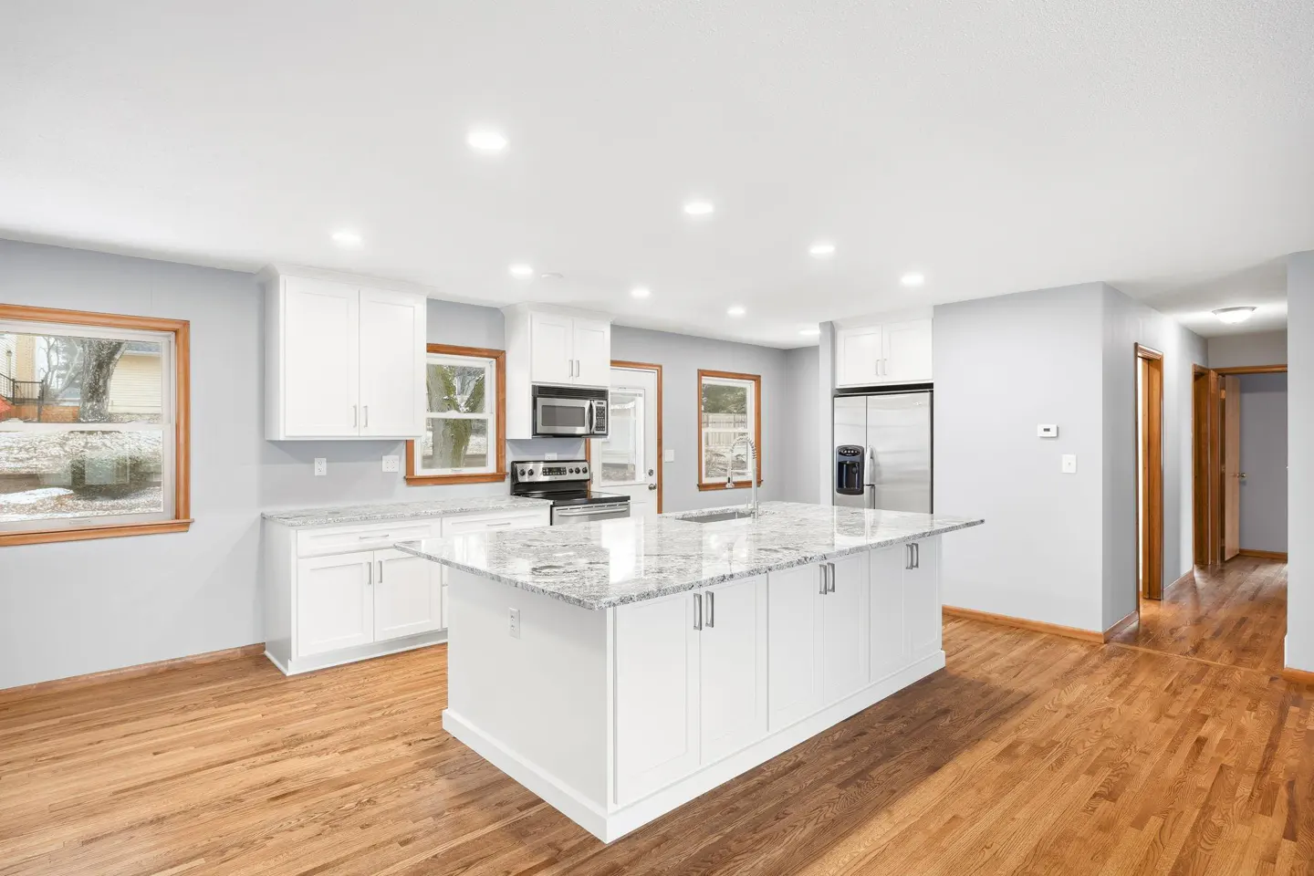 Bright kitchen with white cabinets, granite countertops, and a large island. Hardwood floors and natural light from windows.