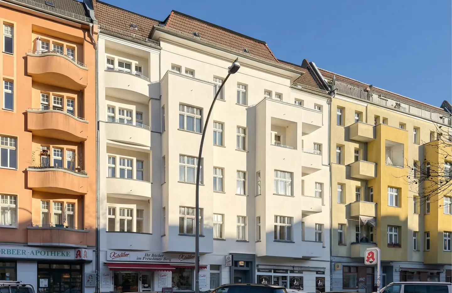 Street view of colorful apartment buildings with balconies and shops on the ground floor on a sunny day.