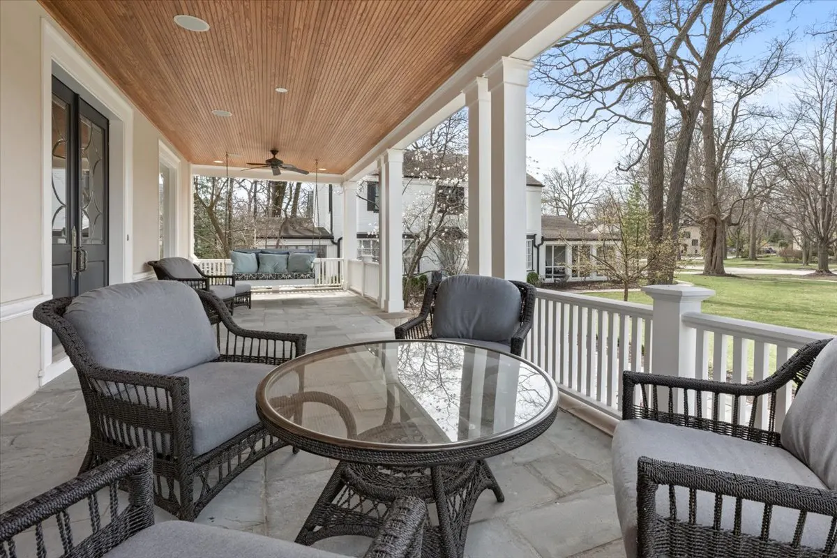Covered porch with wicker furniture, including chairs and a glass-topped table. A porch swing hangs in the background, overlooking a green lawn.