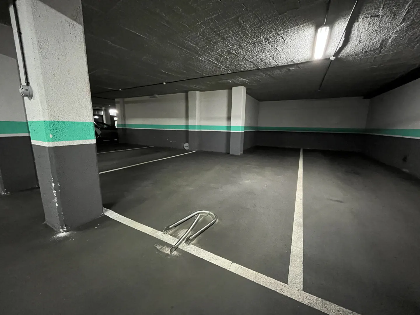 Indoor parking space with gray floor and walls, white parking lines, and a metal wheel chock.