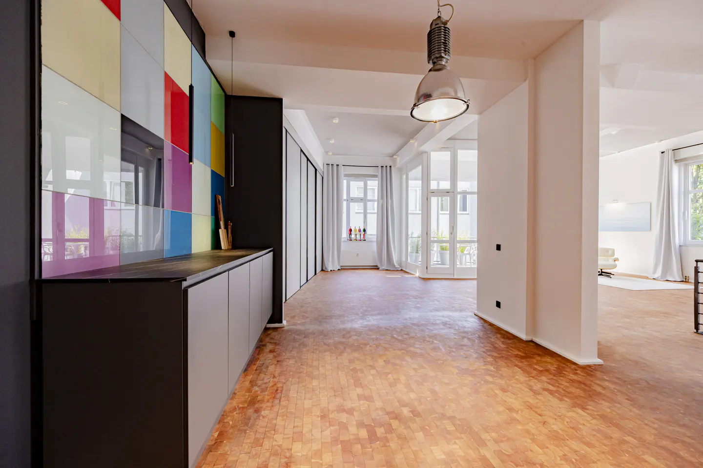 Bright, open apartment with parquet floors. A colorful tiled wall accents the kitchen area. Large windows let in natural light.