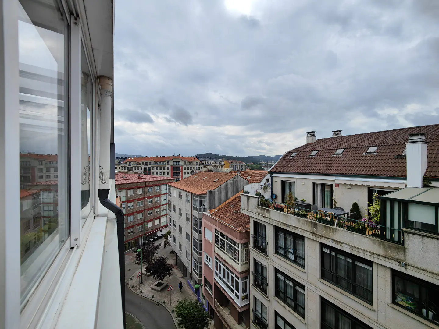 View from a window overlooking a European city with red-tiled roofs under a cloudy sky.