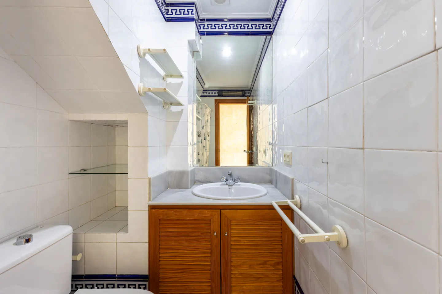 Bathroom with white tiles, blue trim, wood vanity, white sink, and a mirror reflecting a doorway.