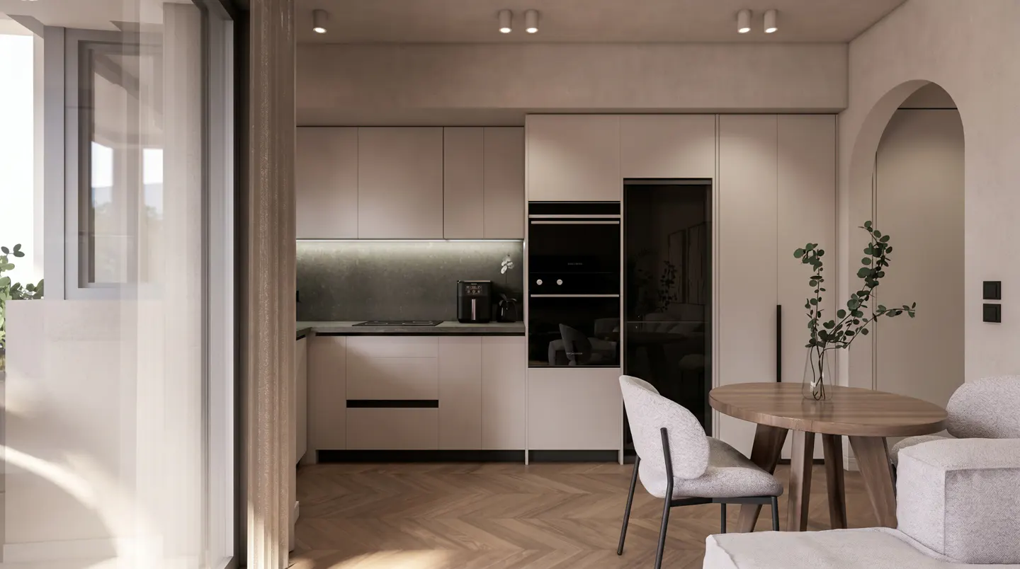 A modern kitchen with light wood floors, white cabinets, and a round wooden table with a vase of greenery. A large window is on the left.